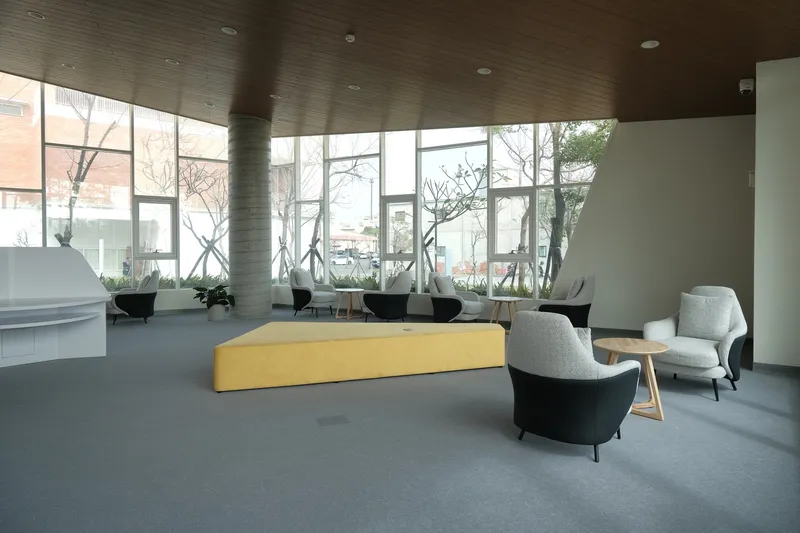 Lounge area with yellow bench seating and grey armchairs beneath timber ceiling and cross-braced glazed wall