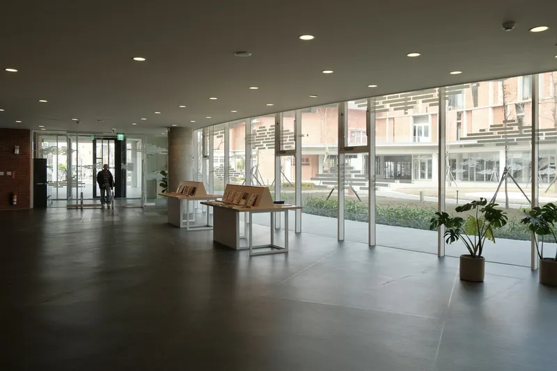 Glass-walled lobby with large-format grey floor tiles and views to the courtyard beyond