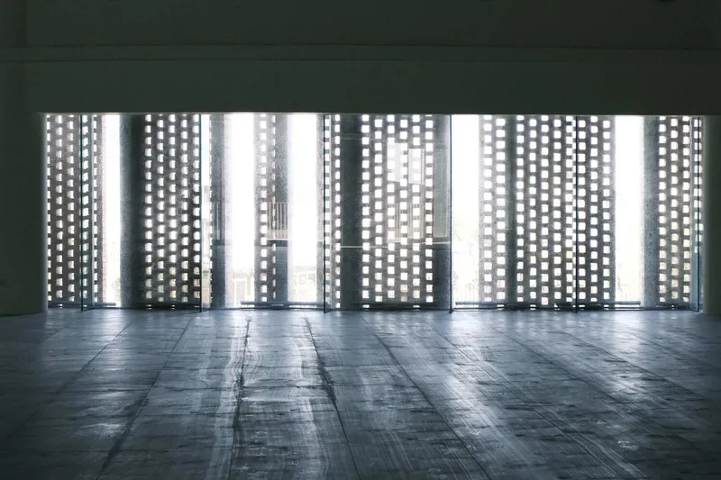 Perforated brick screen wall filtering bright daylight into a darkened interior corridor