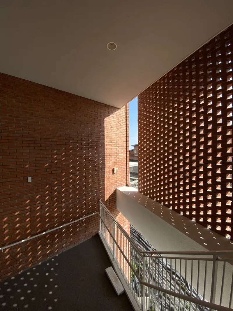 Stairwell flanked by perforated brick walls with sunlight streaming through the openings