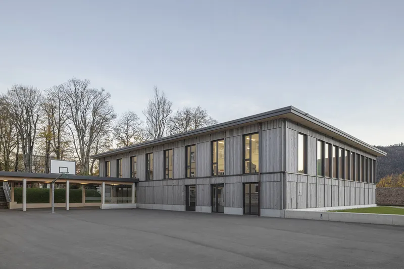 Two-story timber facade with vertical cladding and covered walkway adjacent to asphalt courtyard