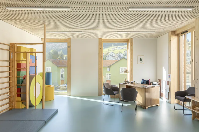 Office or classroom with perforated timber ceiling and windows framing a yellow building across the courtyard