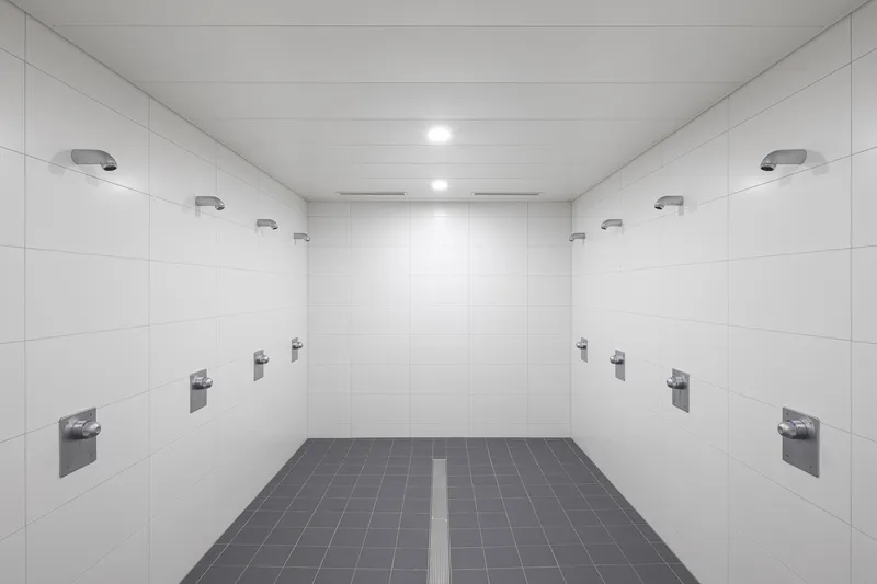 Shower room with white wall tiles, multiple chrome fixtures, and central floor drain