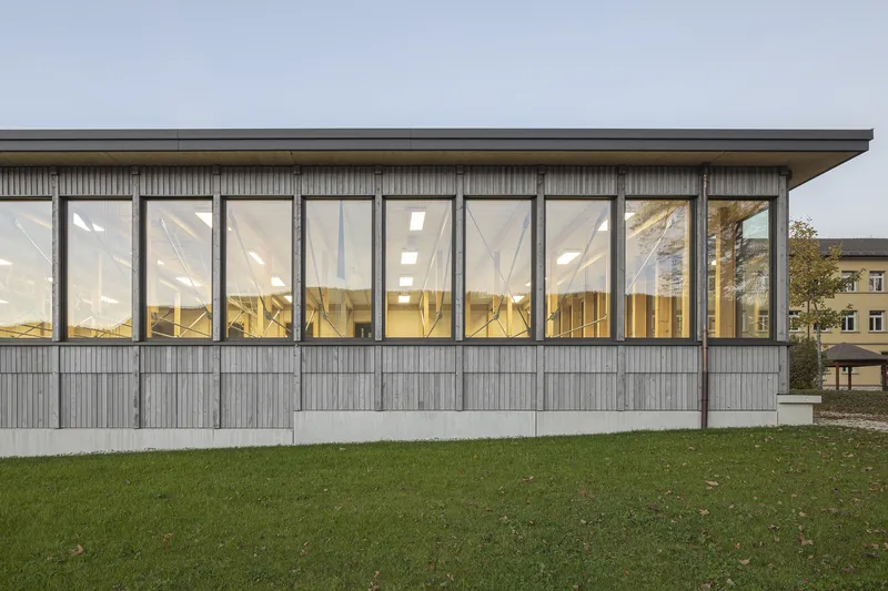 Glazed facade with vertical timber cladding base and timber structure visible through windows at dusk