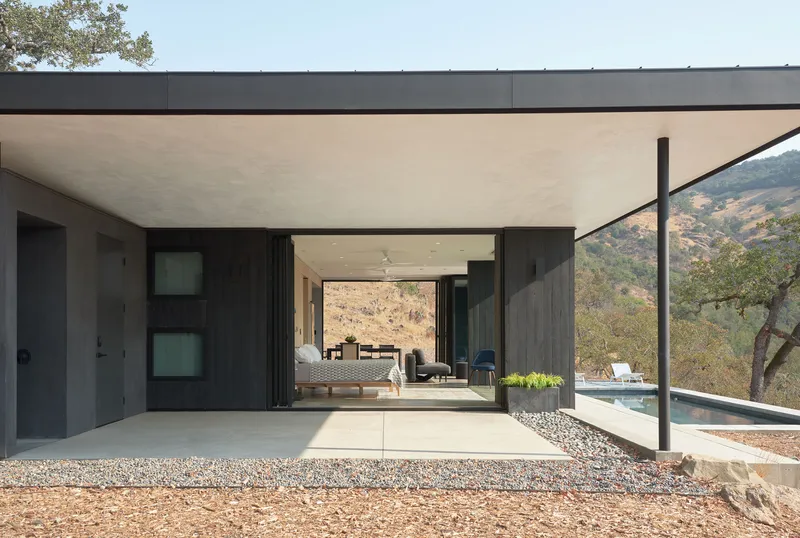 Covered terrace with plywood soffit and folding glass doors opening to pool and hillside beyond