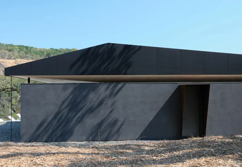 Corner detail showing concrete wall with deep shadow and metal-clad roof soffit in afternoon sun