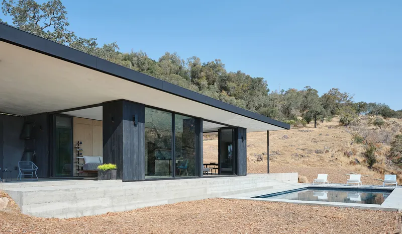 Poolside terrace with concrete edging and cantilevered roof overhang against a dry hillside