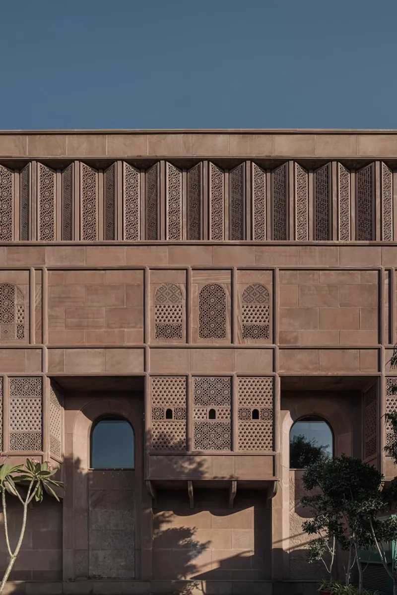 Sandstone facade with geometric latticework panels and arched openings above a planted courtyard
