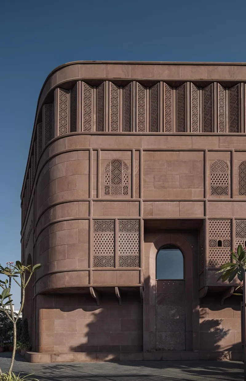 Curved sandstone corner facade with arched entry and ornamental lattice screens under clear sky