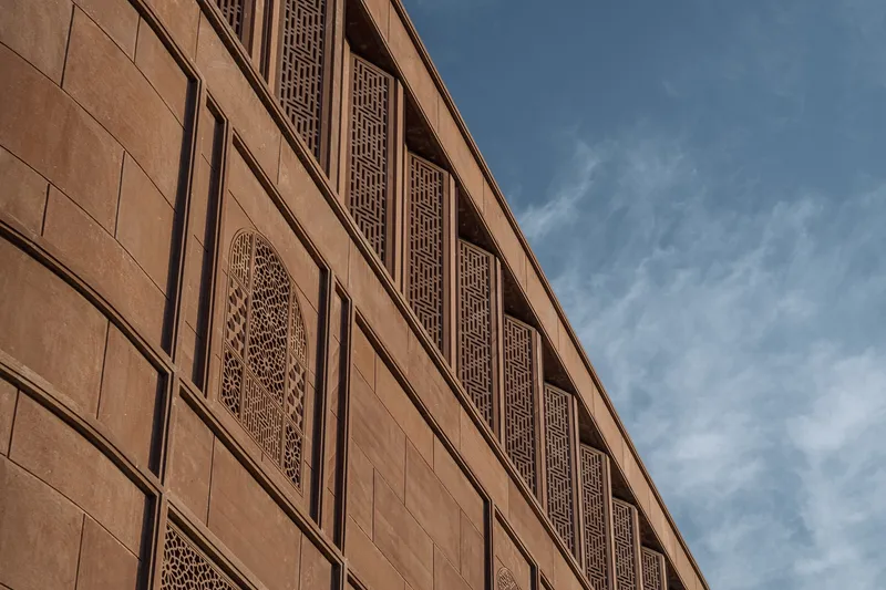 Stone facade with lattice panels and vertical geometric screens under clouded sky
