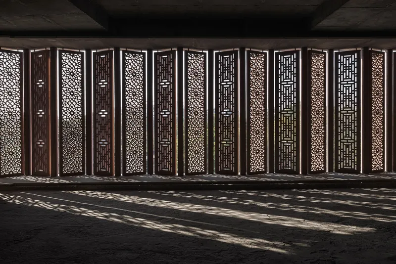 Perforated metal screen wall with alternating geometric patterns casting dappled shadows on the floor below