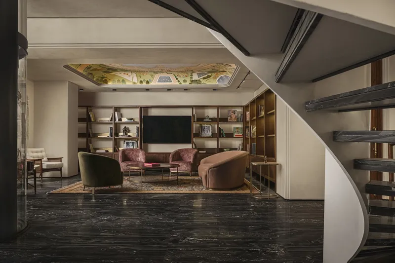 Living room with built-in shelving and painted ceiling mural viewed through a curved staircase opening