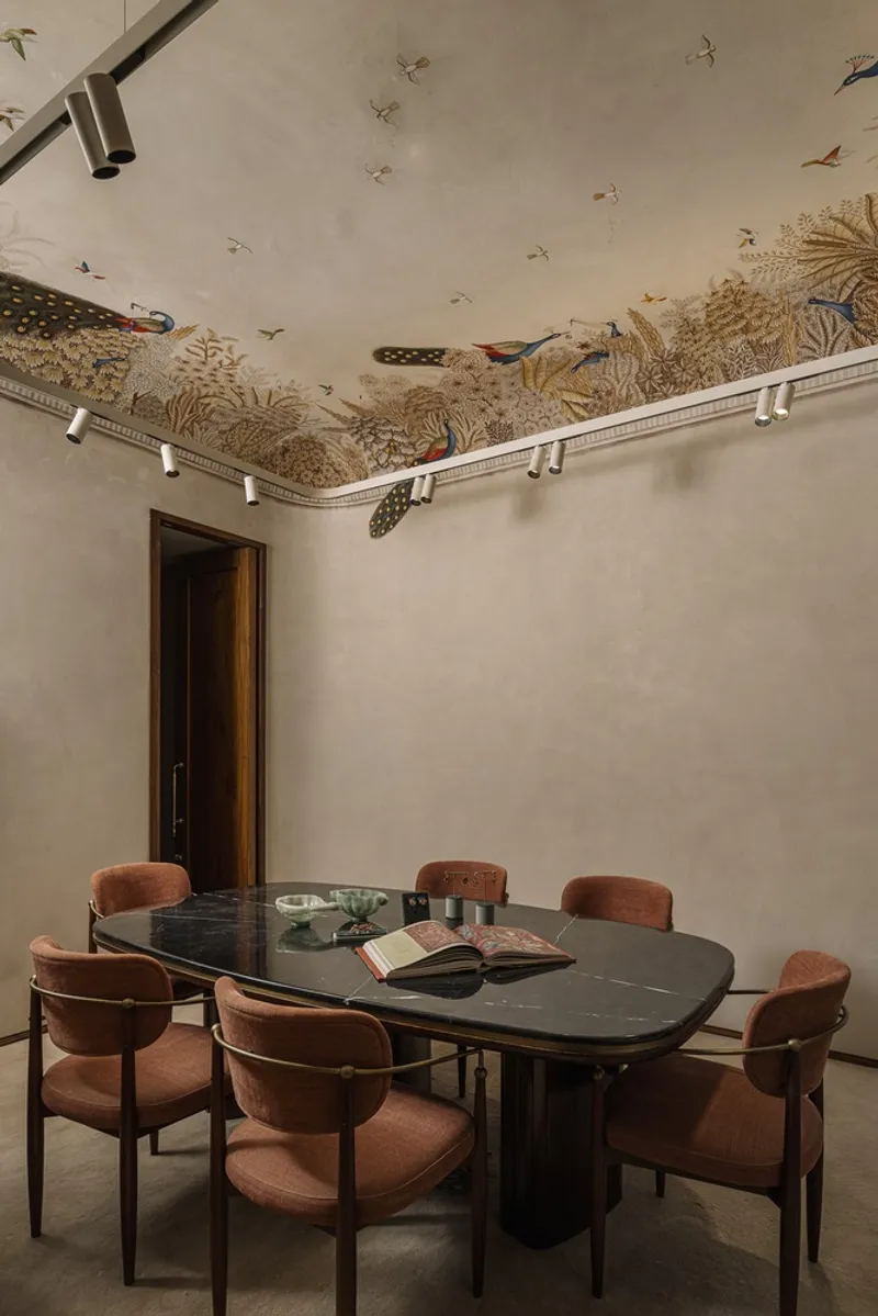 Dining room with dark oval table surrounded by upholstered chairs beneath a hand-painted nature scene ceiling