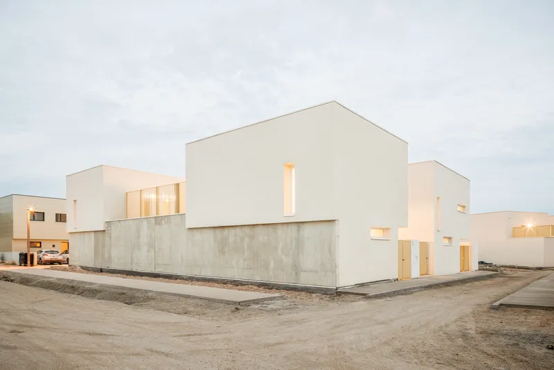 Street view of clustered white stucco volumes with concrete base walls in overcast daylight