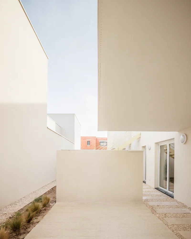 Courtyard with white stucco walls and gravel ground plane with pavers leading to glazed doors