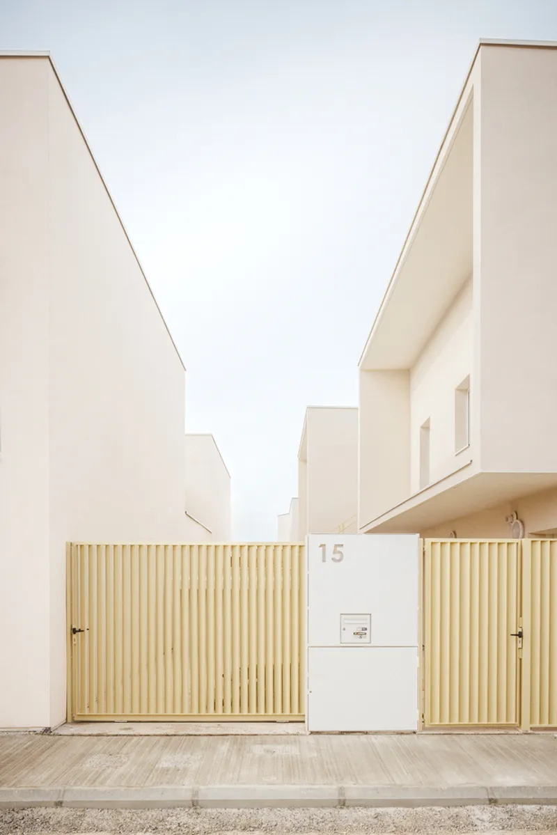 Street view of pale stucco volumes with vertical timber slat gates and house number fifteen