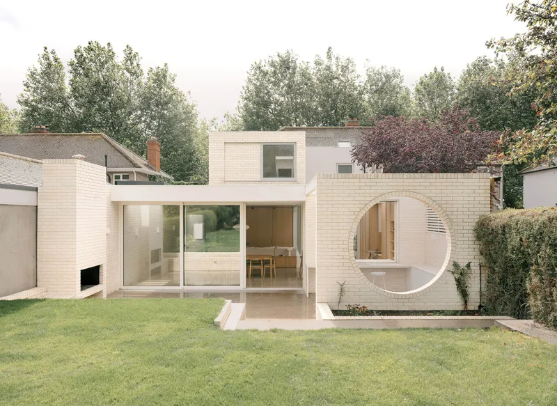 Rear elevation with cream brick facade featuring a circular window opening and full-height glass doors to the garden