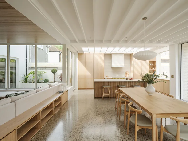 Open-plan kitchen and dining space with exposed ceiling beams and polished concrete floor in afternoon light