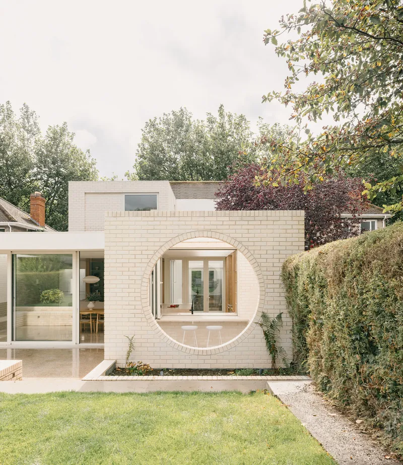 Circular brick opening framing a view through to interior rooms with overcast sky above