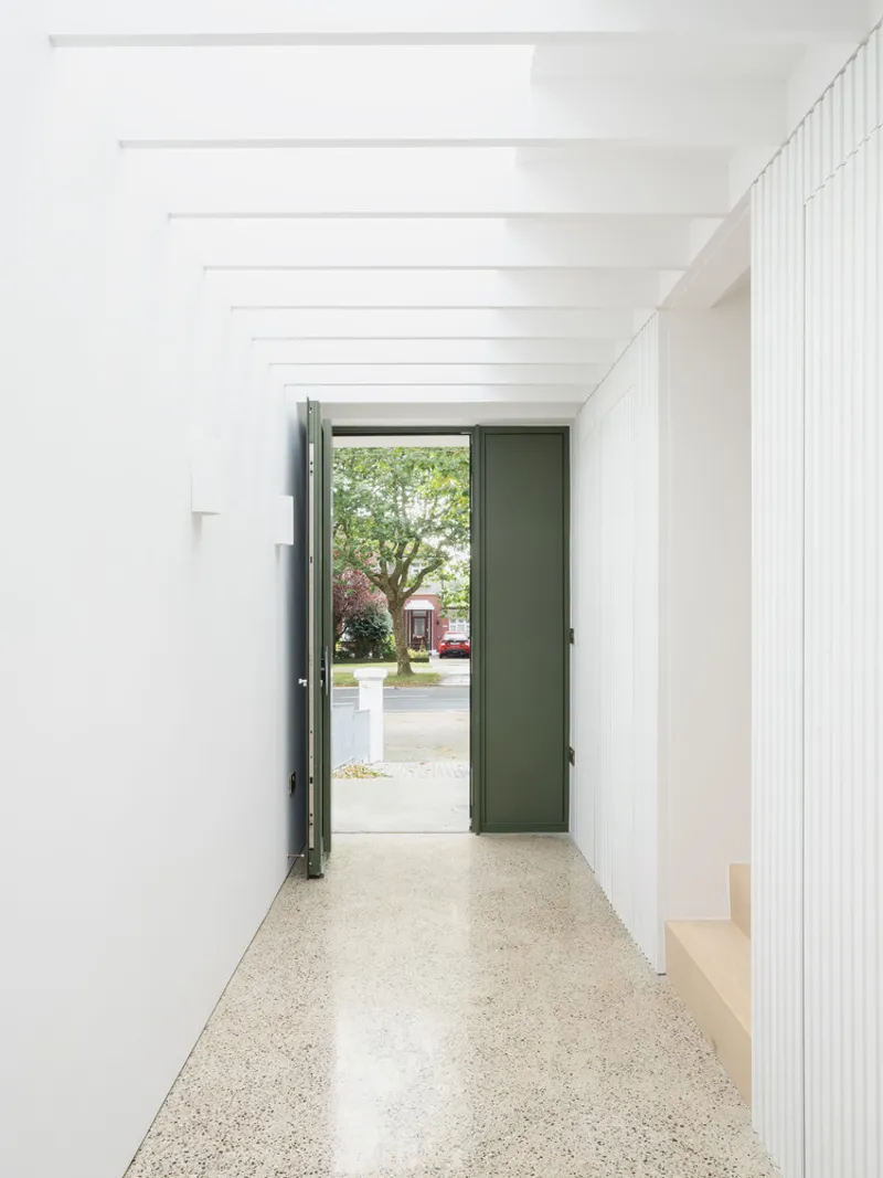 Entry corridor with terrazzo floor and open green door revealing a tree-lined street beyond