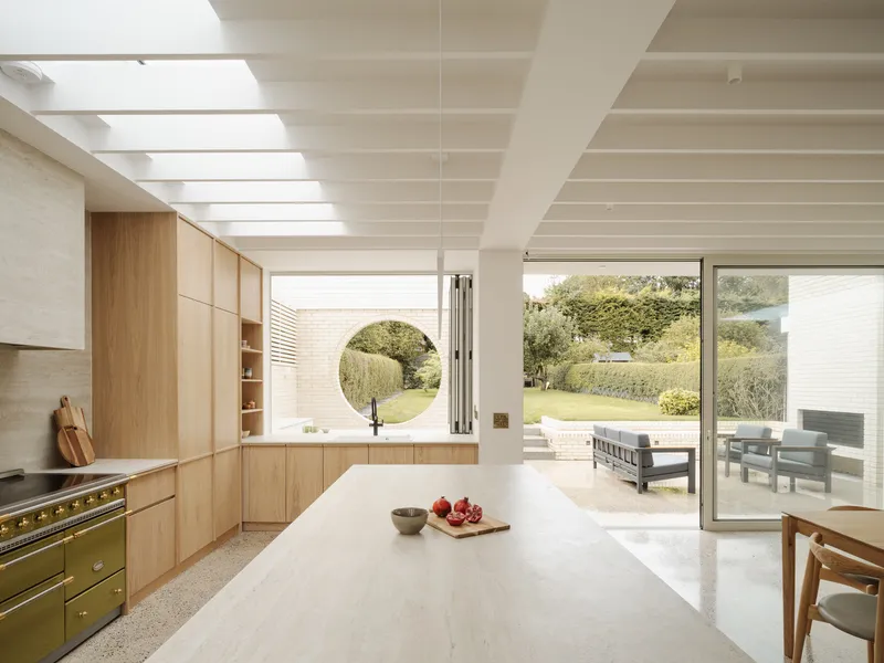Kitchen with oak cabinetry and circular window opening onto the garden under a ribbed skylight ceiling