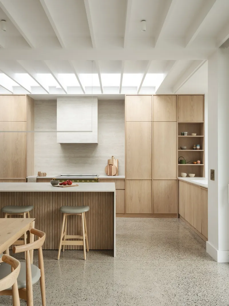 Kitchen island with fluted timber base and terrazzo flooring beneath a white-painted beam and skylight structure