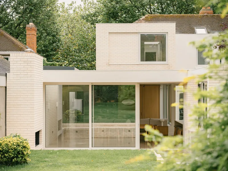Garden view of the pale brick rear extension with floor-to-ceiling glazing framed by mature trees