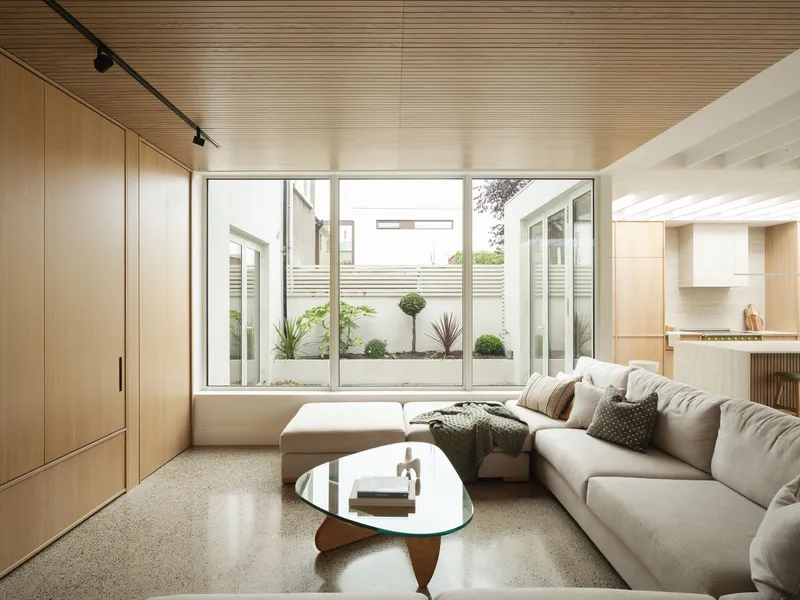 Living room with timber-slatted ceiling and picture window overlooking a planted courtyard with white fencing