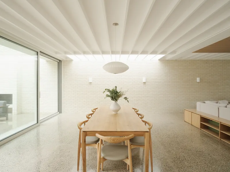 Dining room with pale brick wall and exposed white beam ceiling illuminated by natural daylight