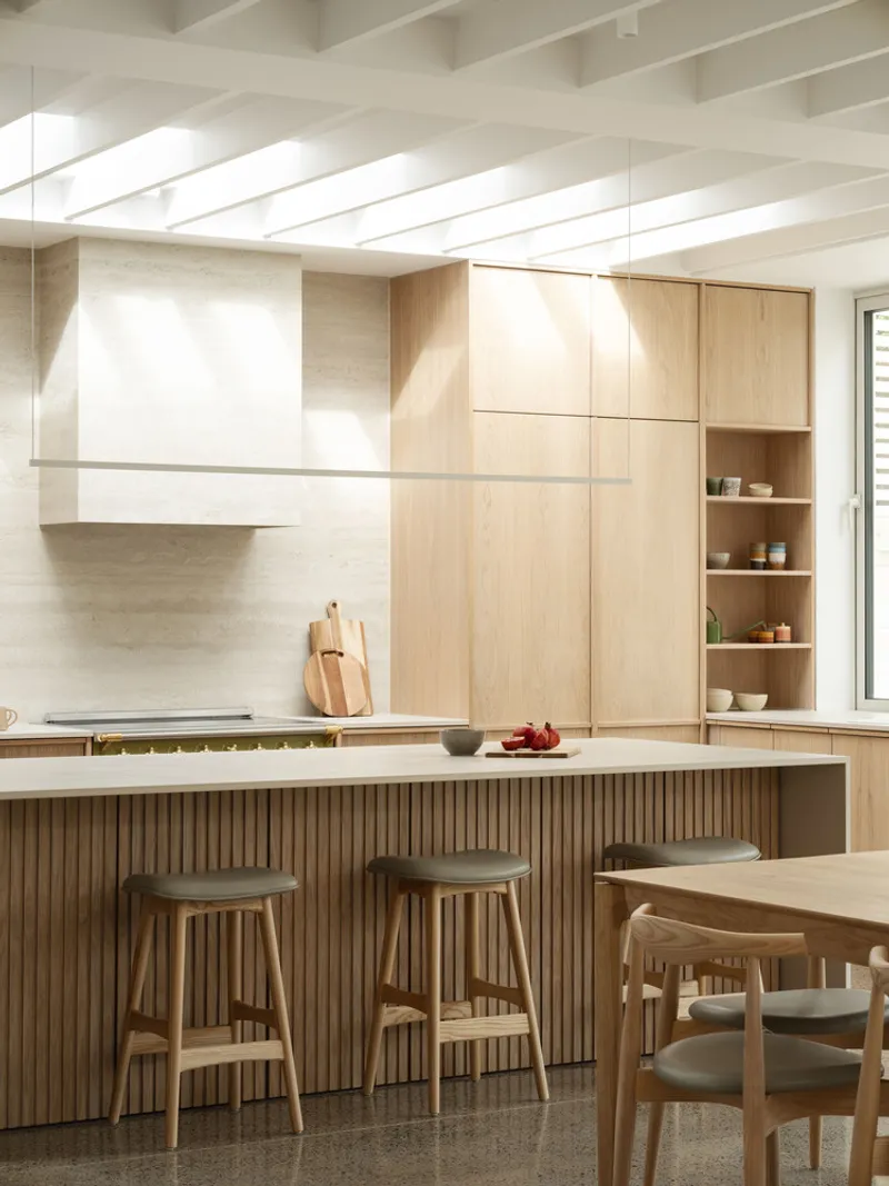 Kitchen with fluted island base, timber bar stools, exposed ceiling joists, and open shelving near window