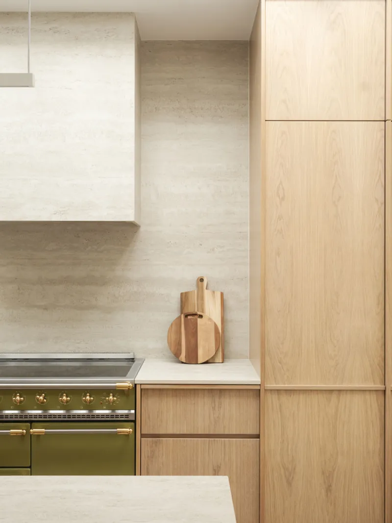 Kitchen detail showing pale stone backsplash, olive green range, and light oak cabinetry with cutting boards