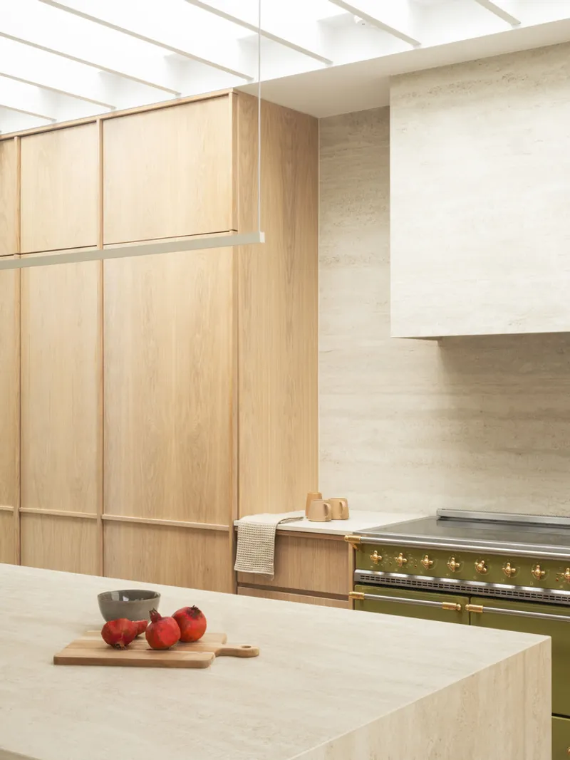 Kitchen island with pale stone countertop, exposed timber ceiling beams, and oak wall cabinetry above range