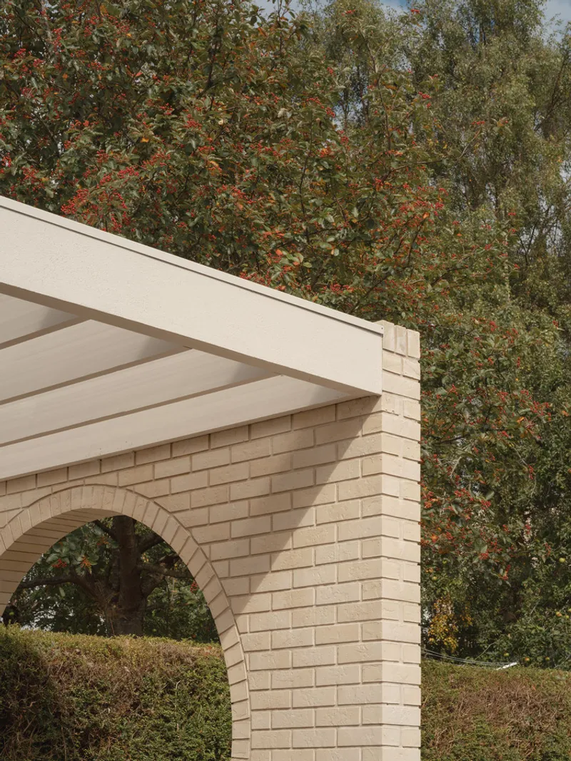 Exterior view of pale brick archway and flat roof soffit against dense foliage