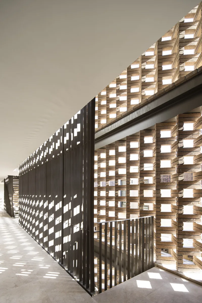 Interior corridor with perforated dark metal screens casting dappled light onto concrete floors