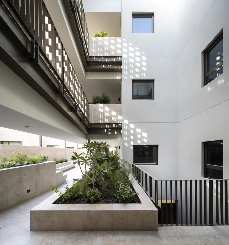 Central courtyard with raised concrete planter, vertical metal slat balconies and scattered greenery