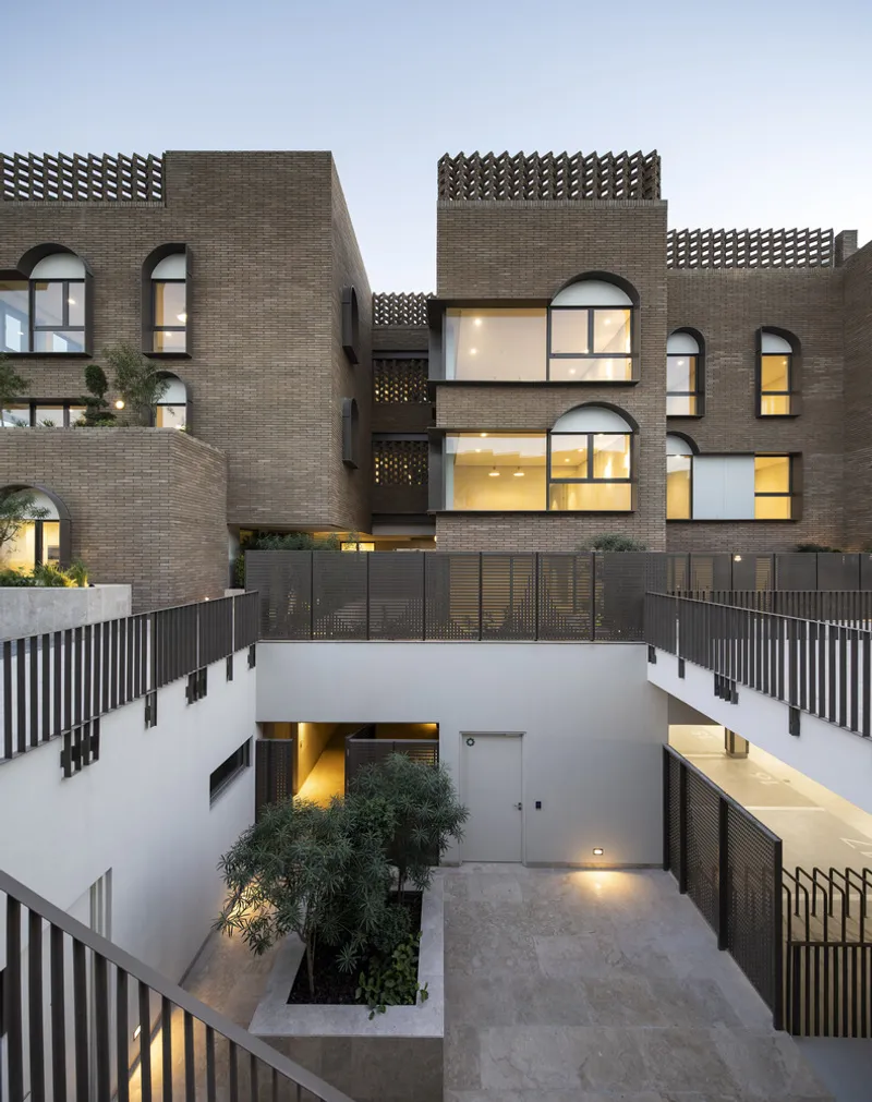 Multi-level courtyard at dusk showing brick facades with arched windows and perforated parapet screens