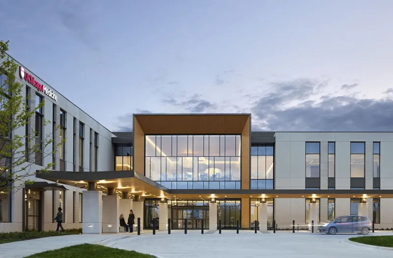 Front entrance with canopy, glazed timber-clad volume and figures at dusk