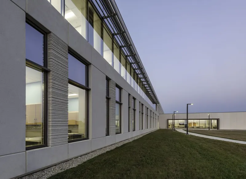 Side elevation with vertical ribbed panels between windows and gravel drainage strip at dusk