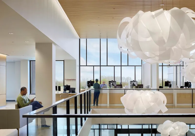Lobby interior with timber slat ceiling, sculptural pendant lights and seated figure at window desk