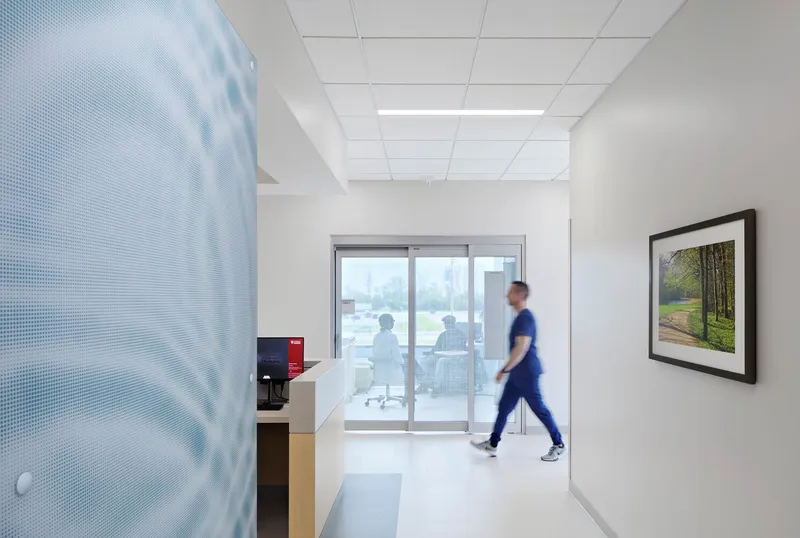 White corridor with perforated glass partition and a person walking past glazed offices