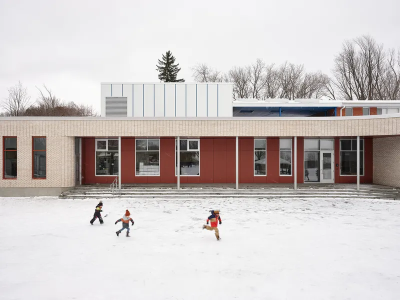 Courtyard elevation with red metal panels and cream brick as children play in the snow