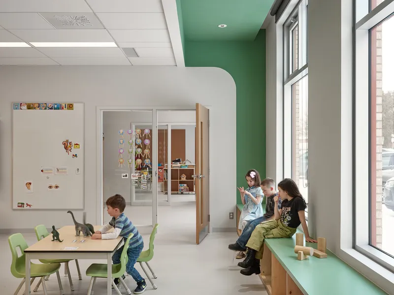 Interior play area with green ceiling accent and children seated on a window bench by glazed walls