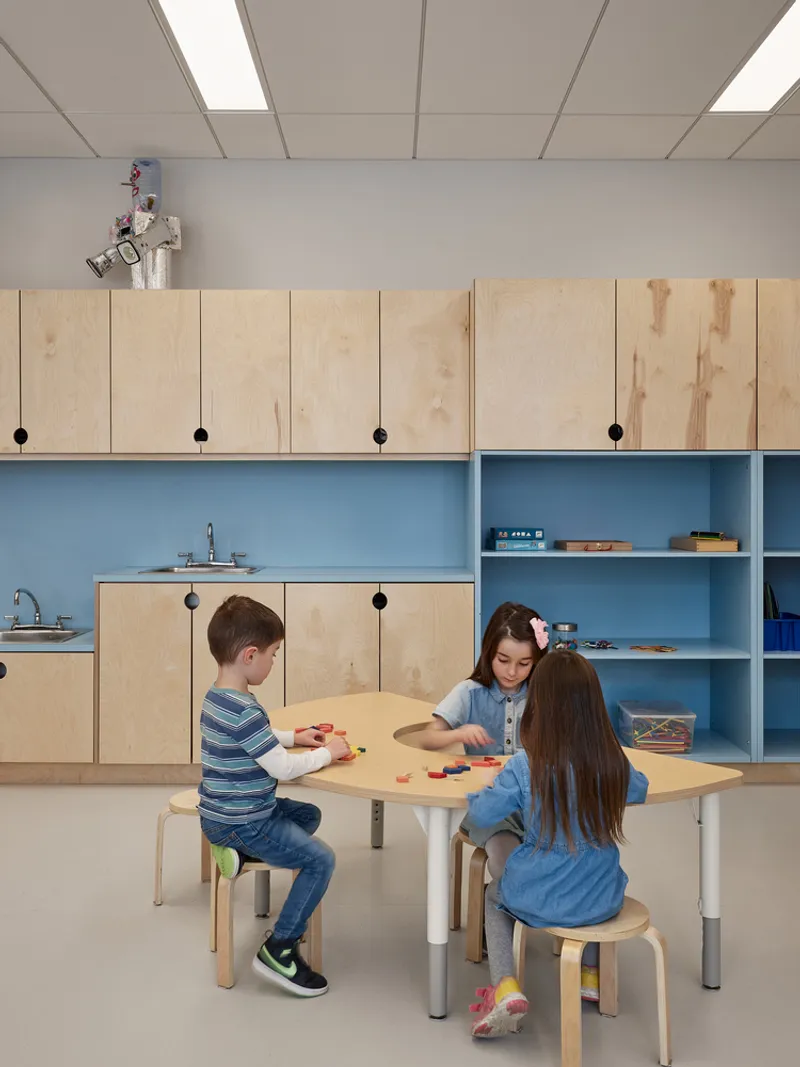 Birch plywood cabinetry with blue shelving and children seated at a low activity table