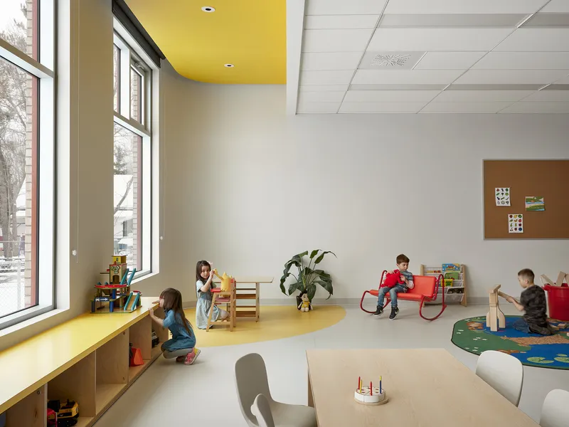 Classroom interior with yellow ceiling panel and curved yellow flooring where children play near tall windows
