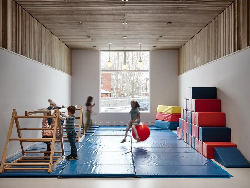 Gymnasium room with timber-clad ceiling and walls above padded play mats where children use climbing equipment