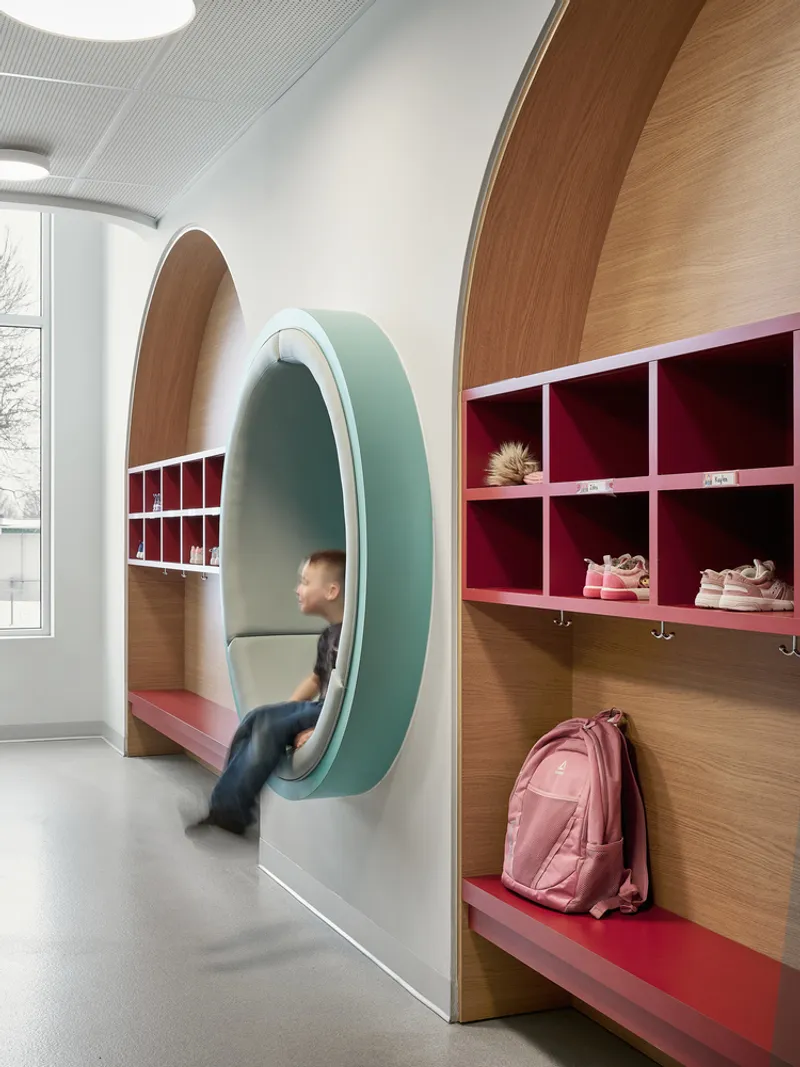 Egg-shaped timber-framed reading alcove set into wall beside storage cubbies with pink accents and hooks