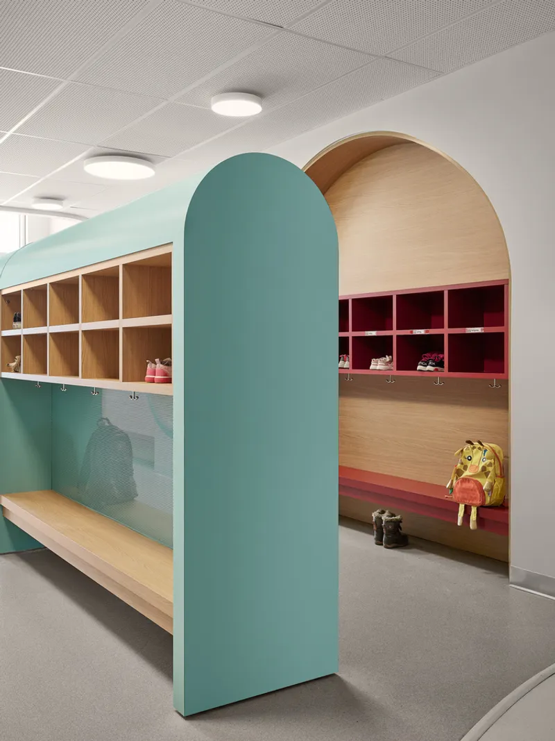 Teal arched partition dividing storage cubby benches with coat hooks and a yellow backpack on the floor