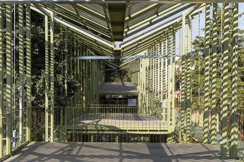 Stacked walkways and platforms enclosed by pale green vertical steel louvers in dappled afternoon light