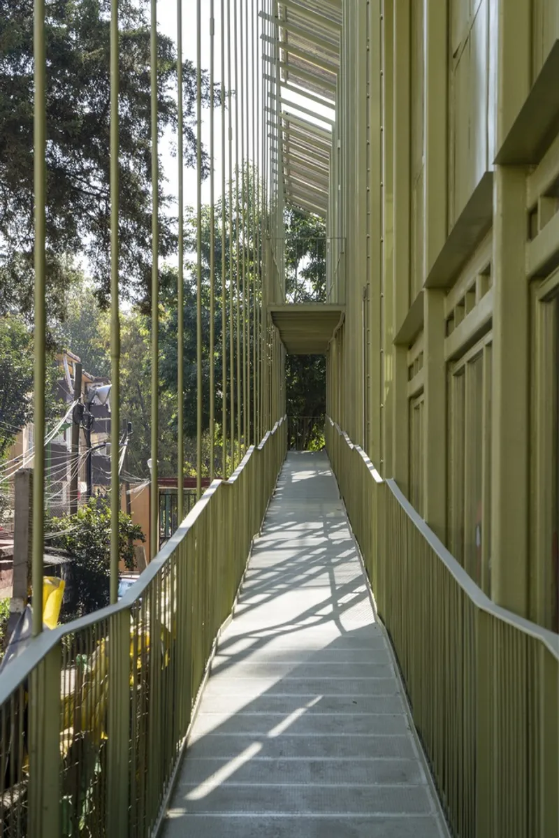Narrow pedestrian bridge flanked by vertical steel slats casting linear shadows across the concrete deck