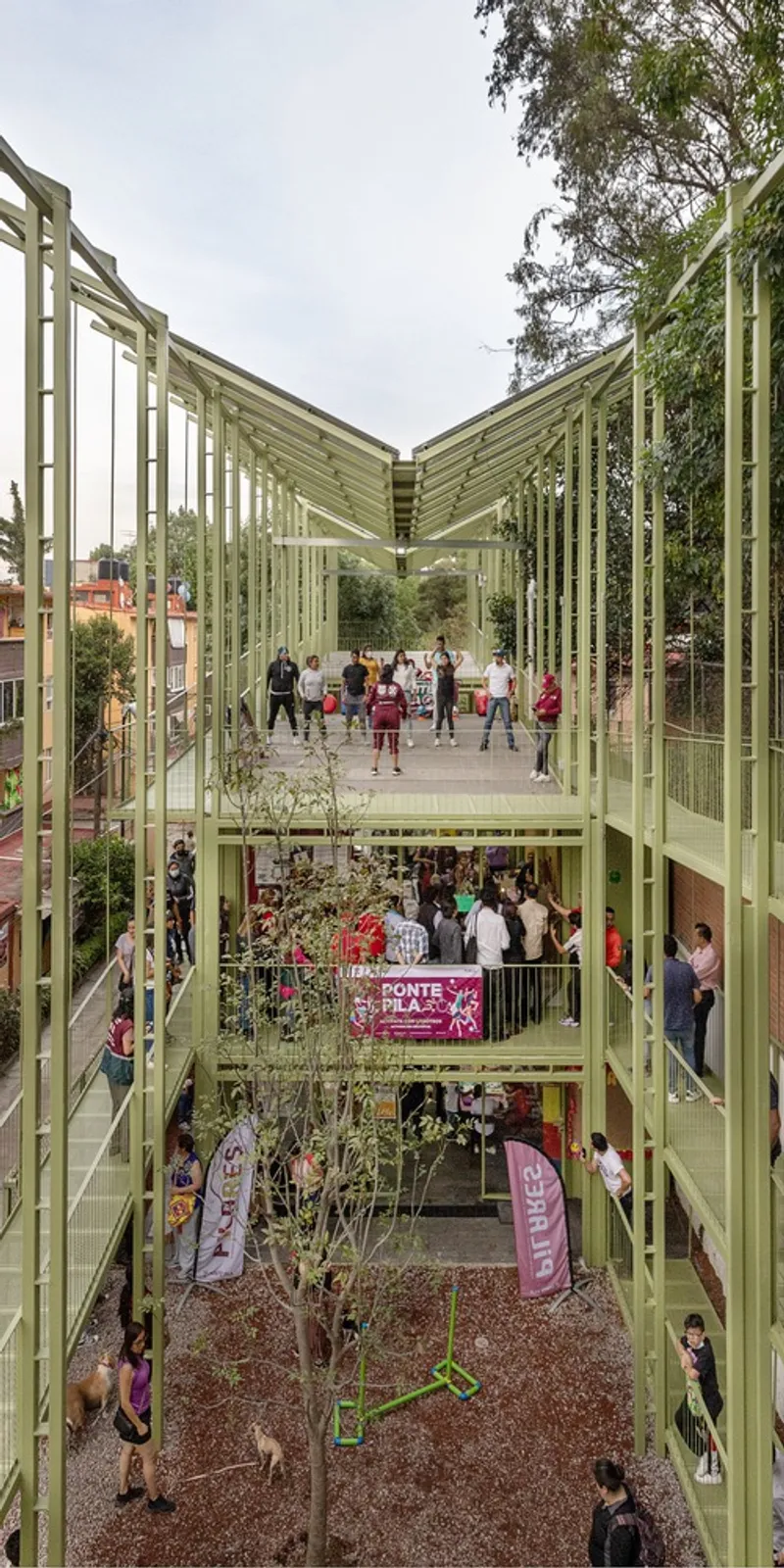 Multi-level view through the V-shaped canopy showing children on upper and lower courtyards at dusk